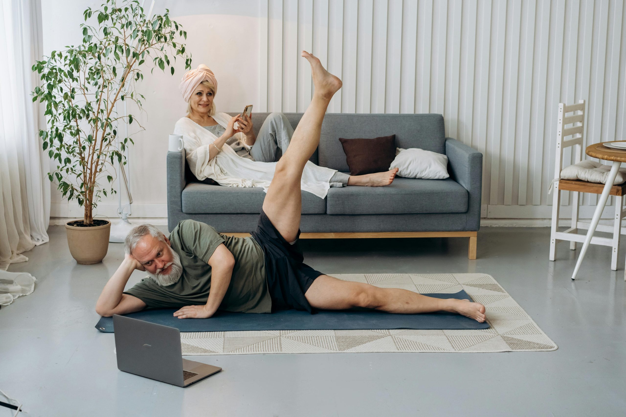 A smiling senior woman practicing seated yoga poses in a sunlit living room